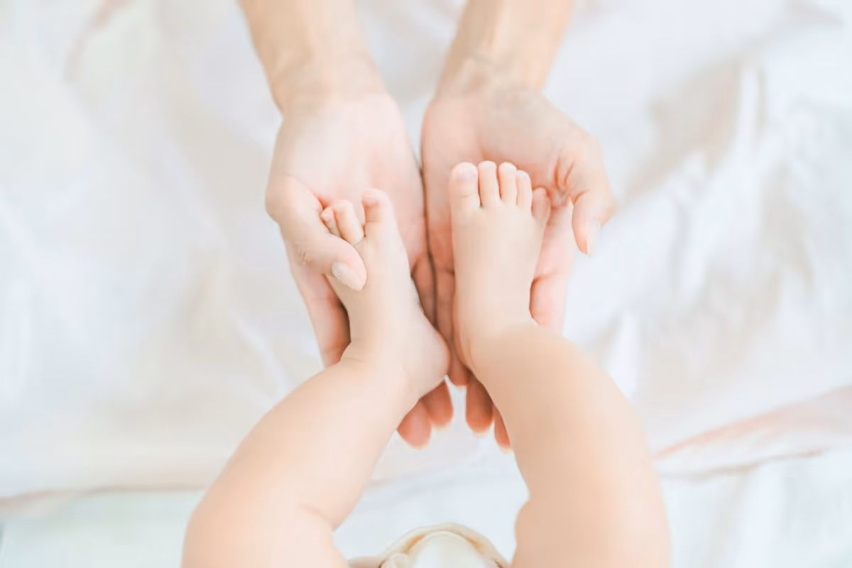 A close-up, overhead shot of a pair of adult hands gently cupping a baby's feet on a white blanket.
