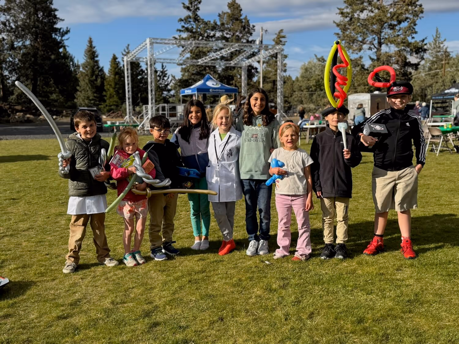 A group of children and a few adults posing for a team photo on a sunny day on a grassy field.