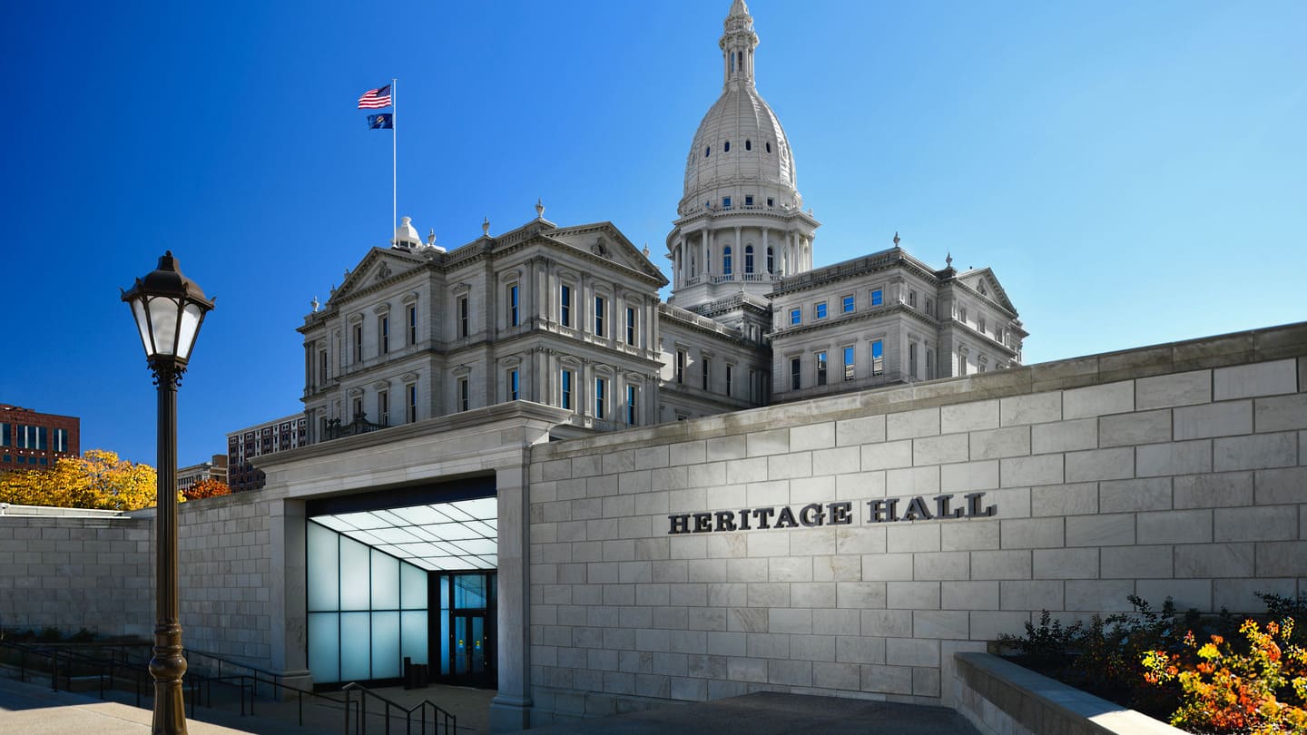 An exterior photo of the entrance to Heritage Hall with the Michigan State Capitol building rising above.
