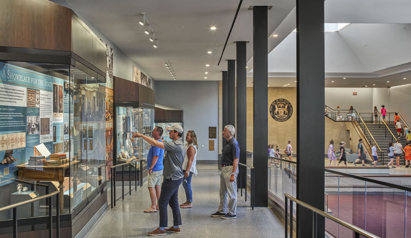 An interior photo of people standing on a ramp and looking at artifacts in cases.