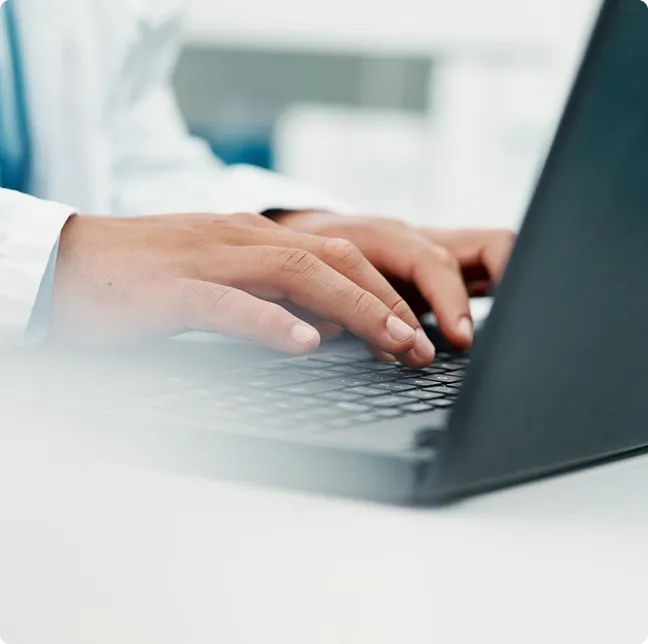 Close-up of hands typing on a laptop keyboard at a workstation.