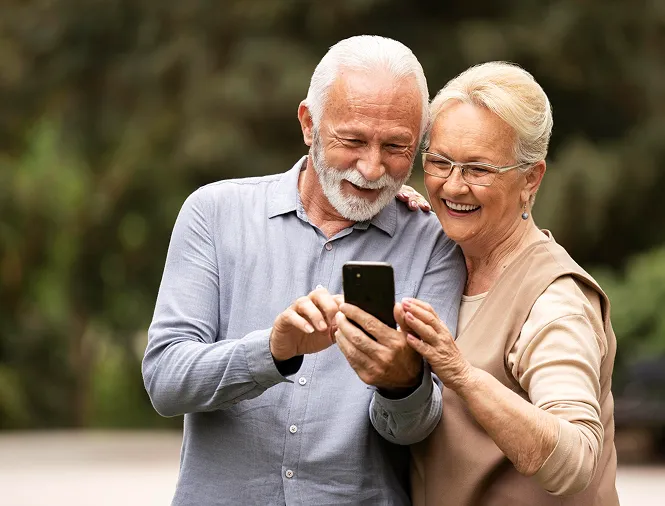 Smiling elderly couple looking at a smartphone together outdoors.