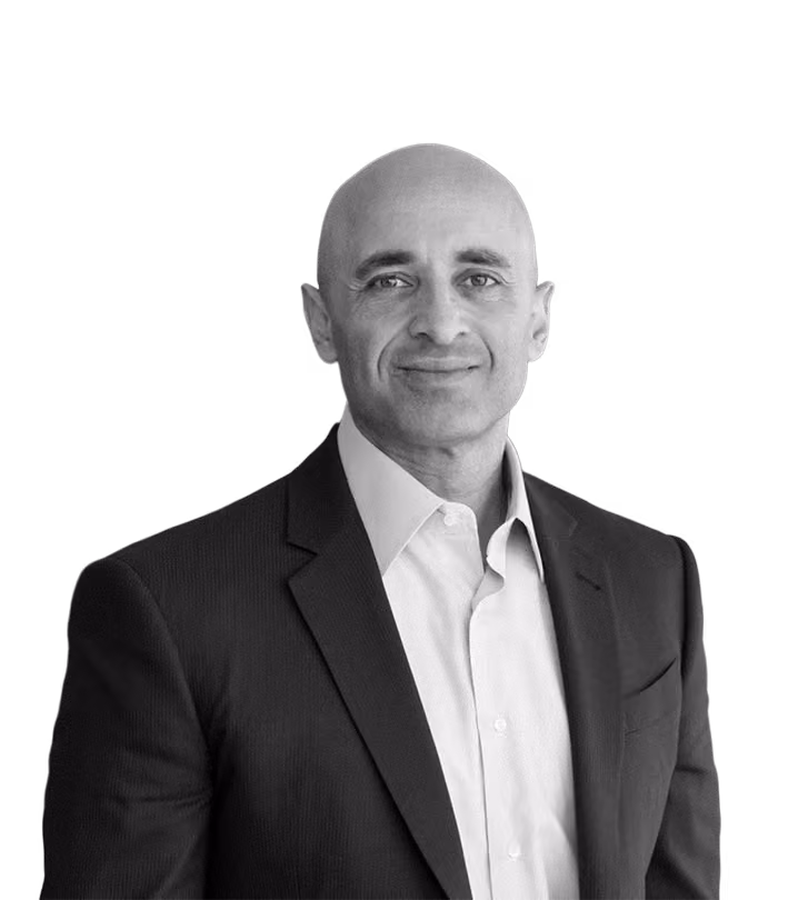Bald man in a dark suit jacket and light dress shirt smiling and looking at the camera.