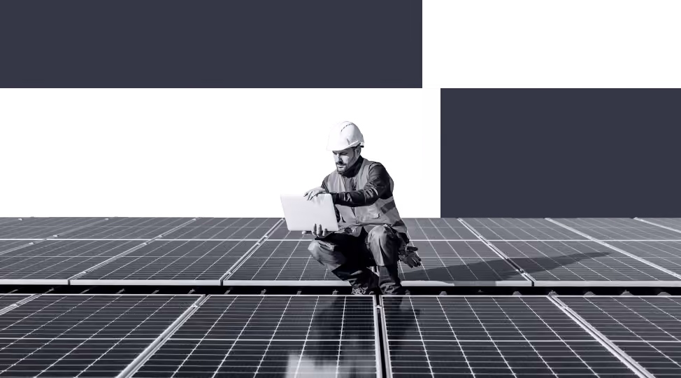 Man in safety gear inspecting solar panels while using a laptop.