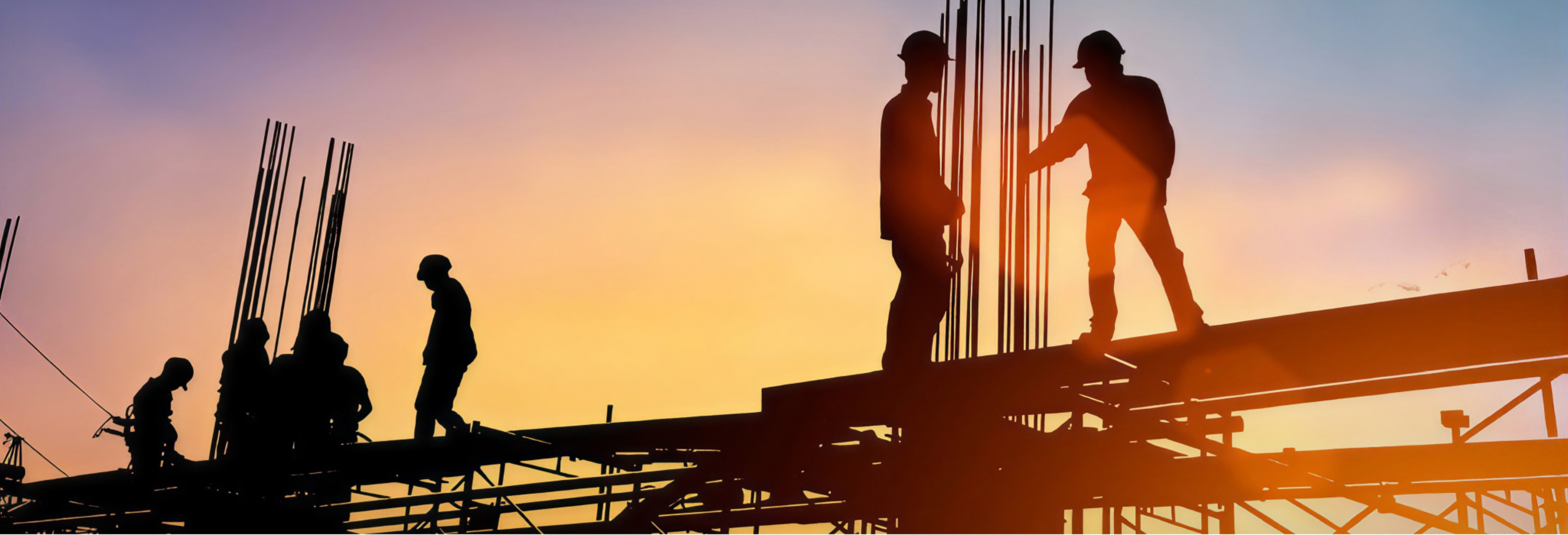 Construction workers in silhouette on a building frame at sunset.
