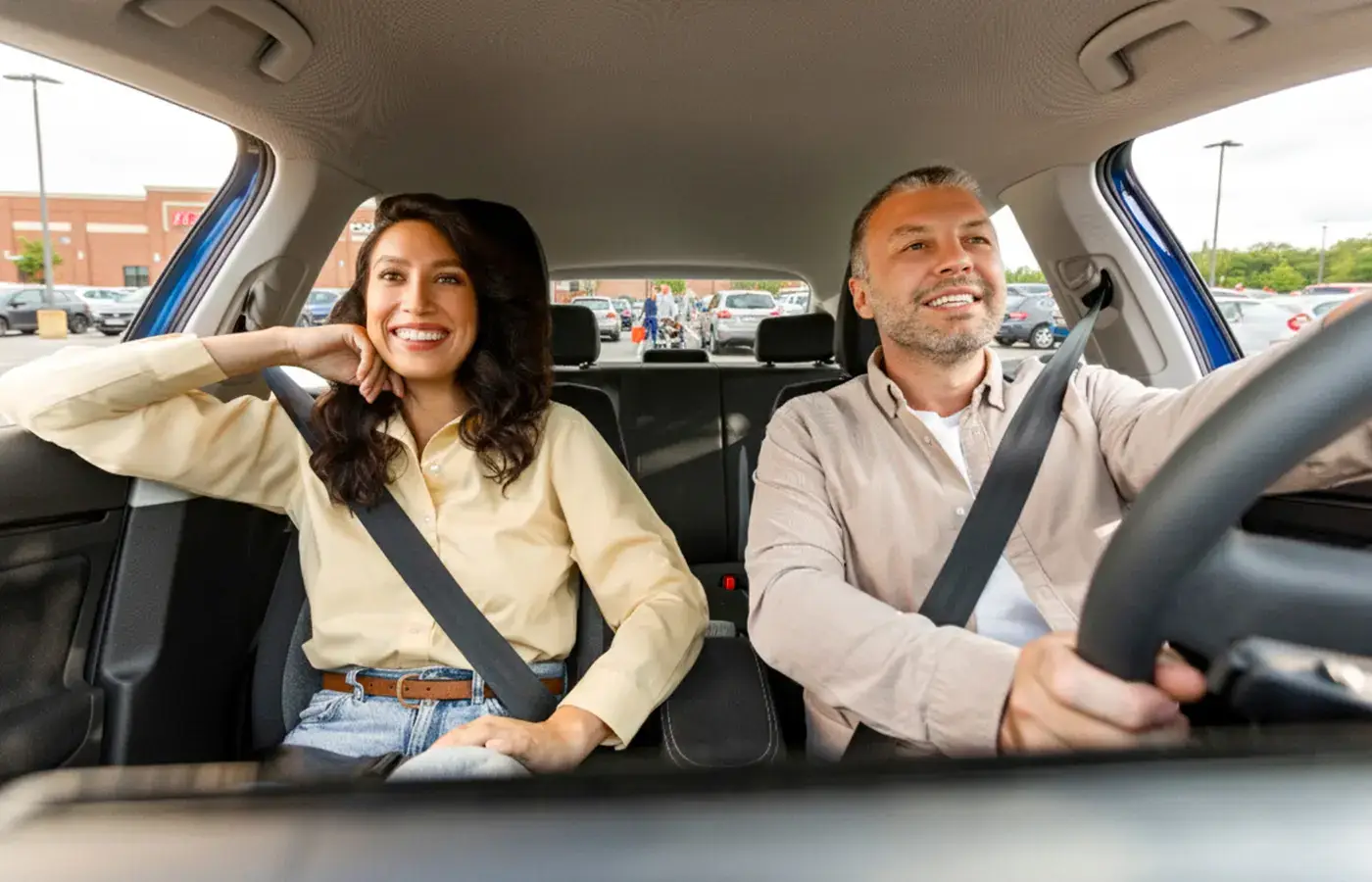 Man driving a car with a smiling woman in the passenger seat during a test drive.