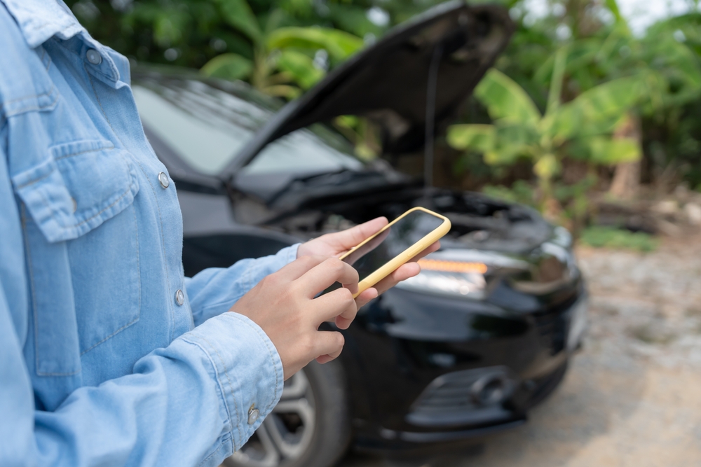 Car owner using a smartphone beside a vehicle with its bonnet open.