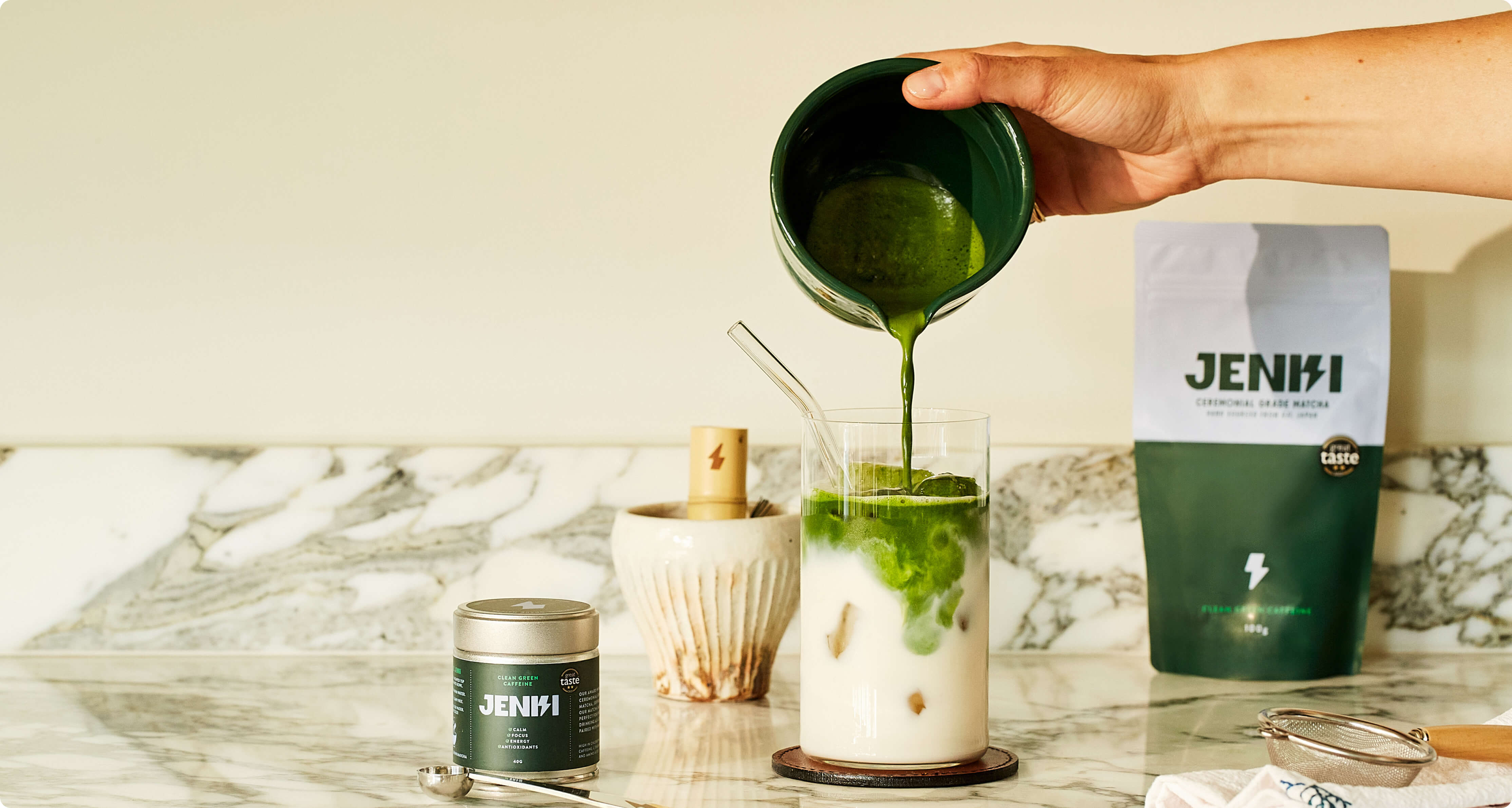 Matcha being poured over milk beside a JENKI matcha tin