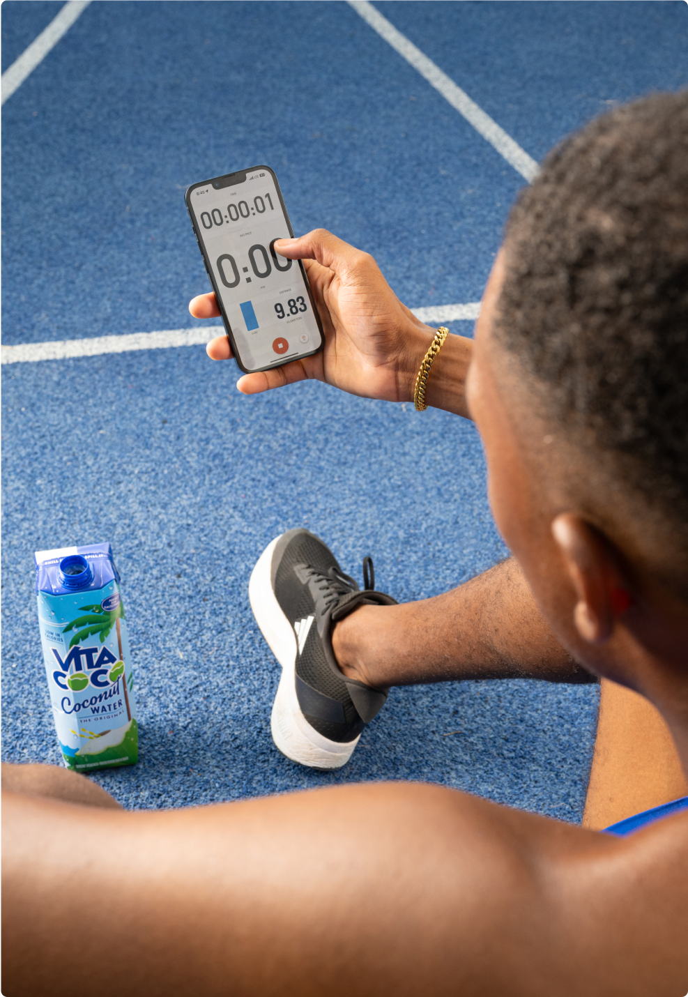 Athlete on a running track holding a phone and a Vita Coco carton