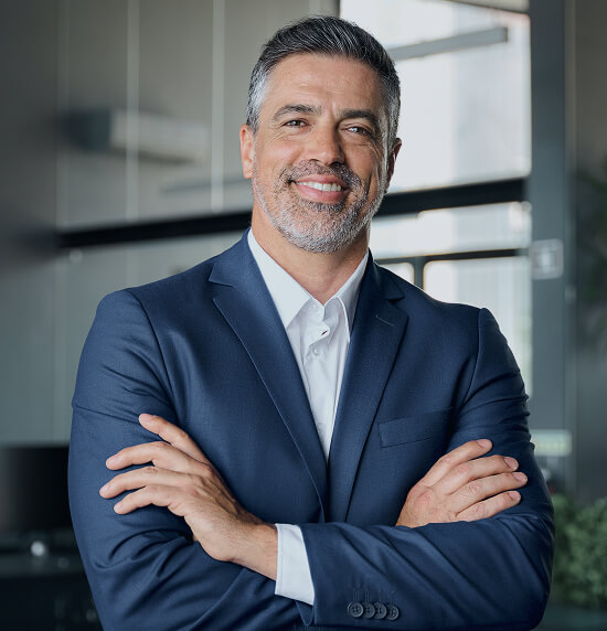 Man in suit standing, looking at camera, with his arms crossed in front of him.