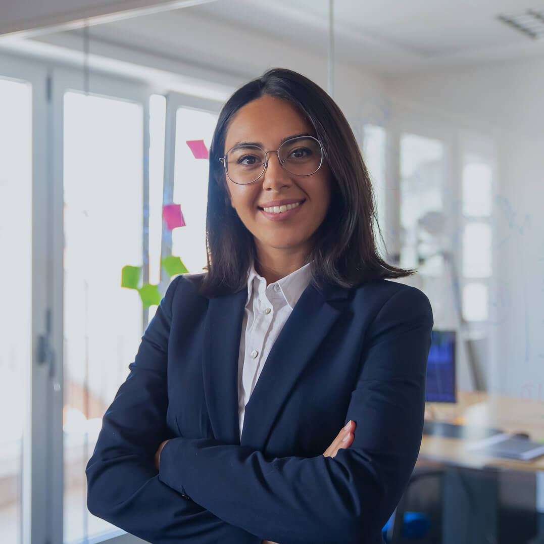 Female lawyer standing with arms folded over her chest in front of her desk.