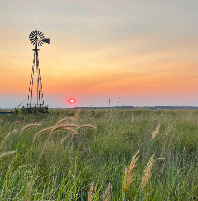 A prairie horizon at dawn with a windmill silhouetted against the sky.
