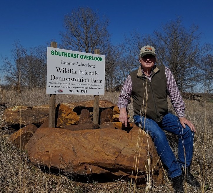 Ron Klataske sits on a large sandstone at the entrance to the Connie Acterberg Wildlife-Friendly demonstration farm