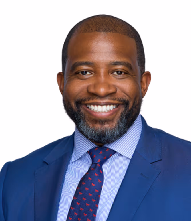 Smiling man with a beard wearing a blue suit jacket, striped shirt, and patterned tie.