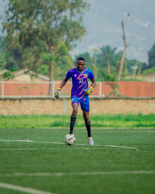 Young goalkeeper in a purple and blue jersey controlling the ball during training