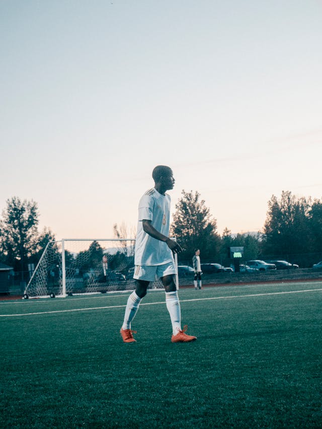 Soccer player in white jersey walking on the field at sunset