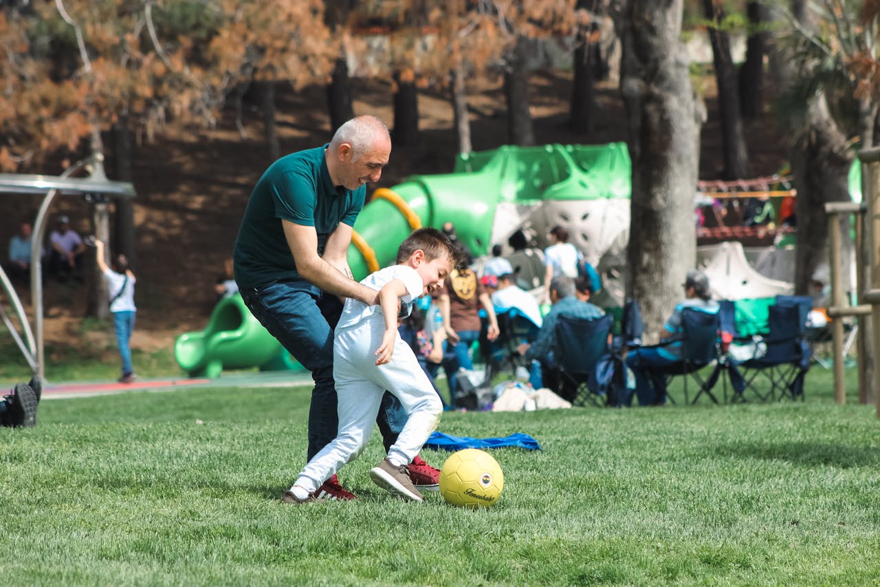 Father and young child playing soccer together on a lush green field, emphasizing parental involvement in youth sports and community engagement at Osner’s FC Academy.