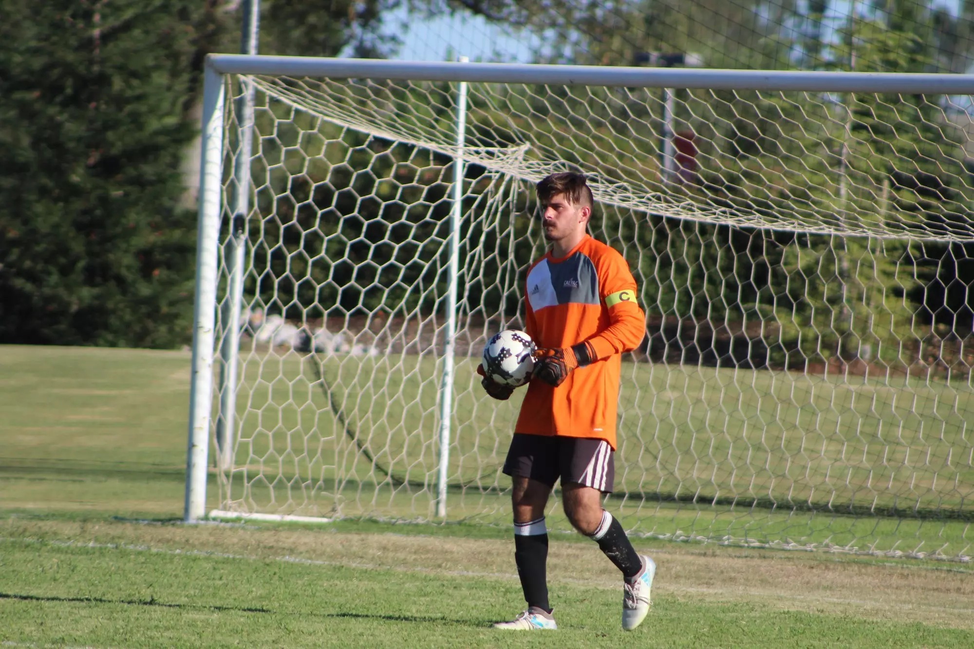 Osner FC goalkeeper in orange kit holding a soccer ball, demonstrating leadership and ready for action at the Fall Break Camp.