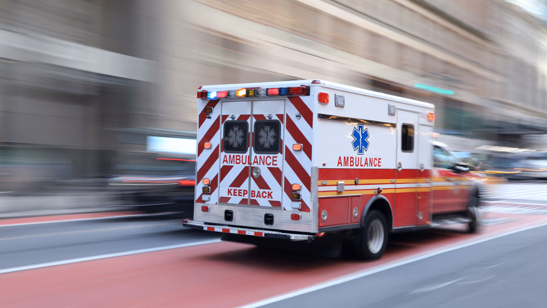 Rear view of a moving emergency ambulance with flashing lights on a city street.