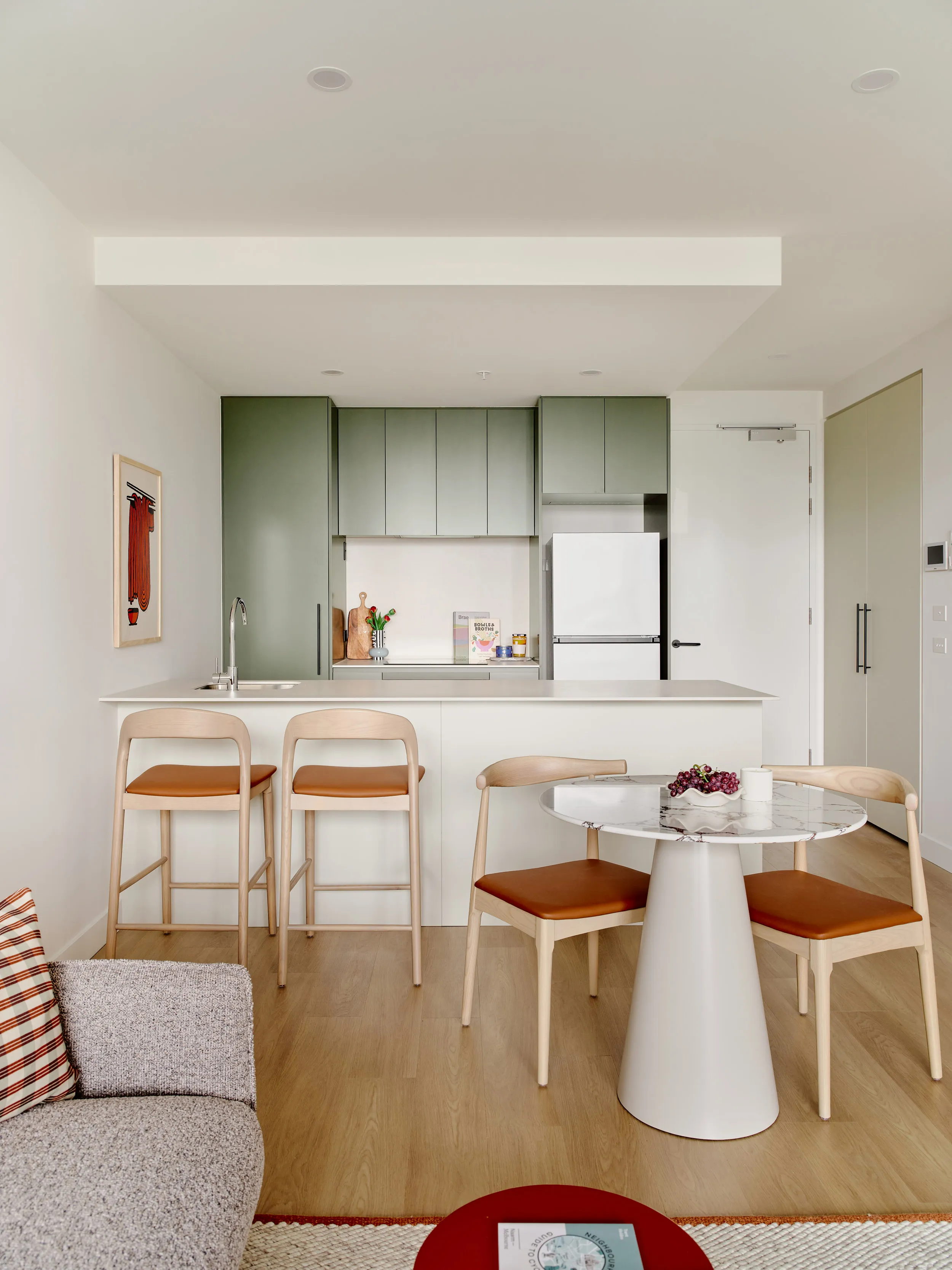 Modern kitchen with green cabinets, white island with stools, a round table, and wooden chairs.