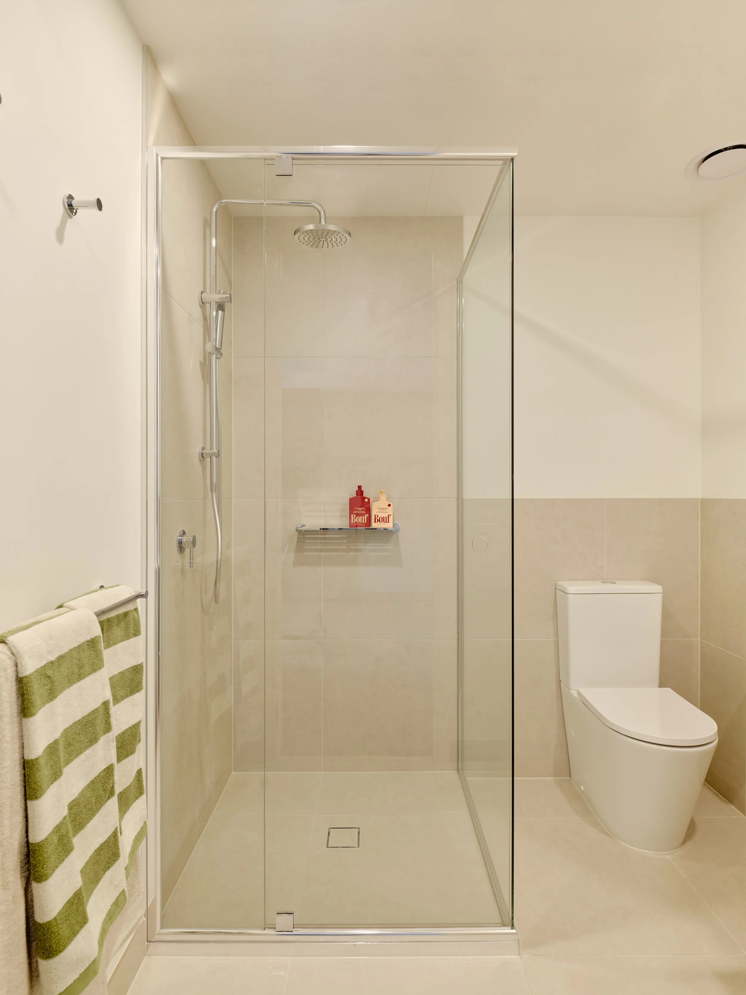 Modern bathroom with a glass shower enclosure, rain showerhead, striped towels, and a white toilet.