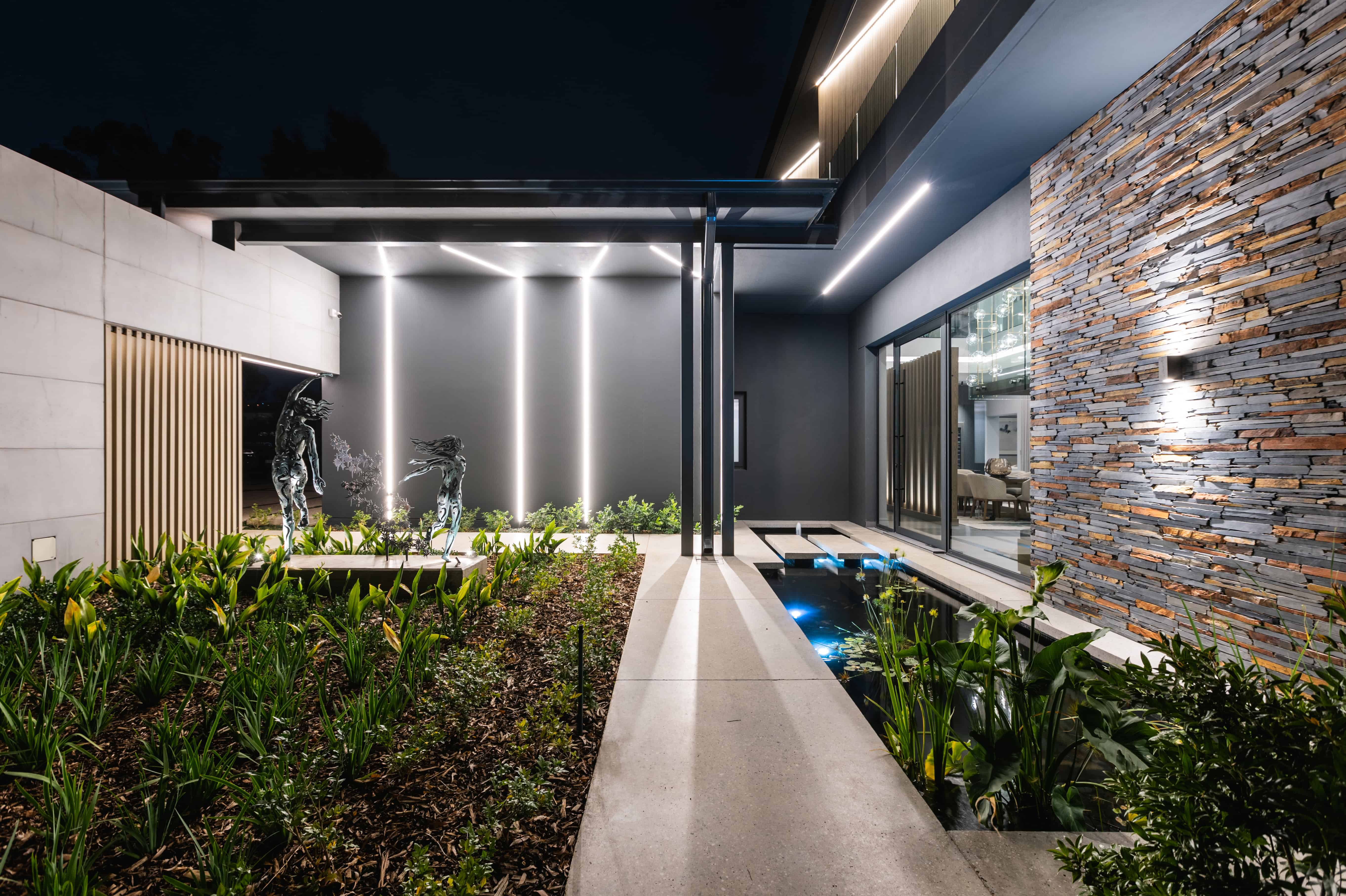 Evening courtyard/entrance with landscaped beds and wall lights, Steyn City luxury home – Renovatio Johannesburg.