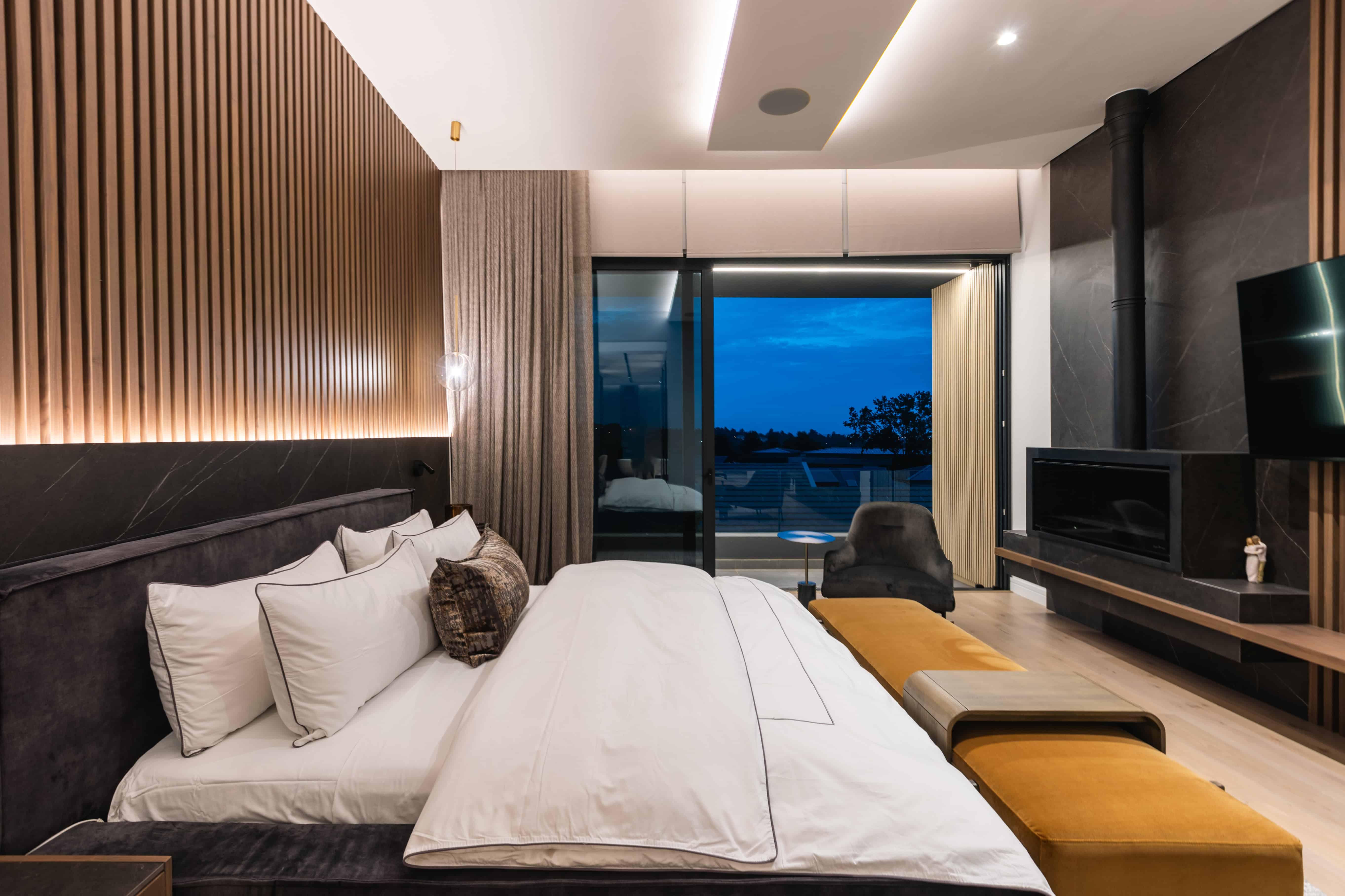 Modern bedroom with timber slat wall, warm tones, and night view over Steyn City, designed by Renovatio Interiors Johannesburg.