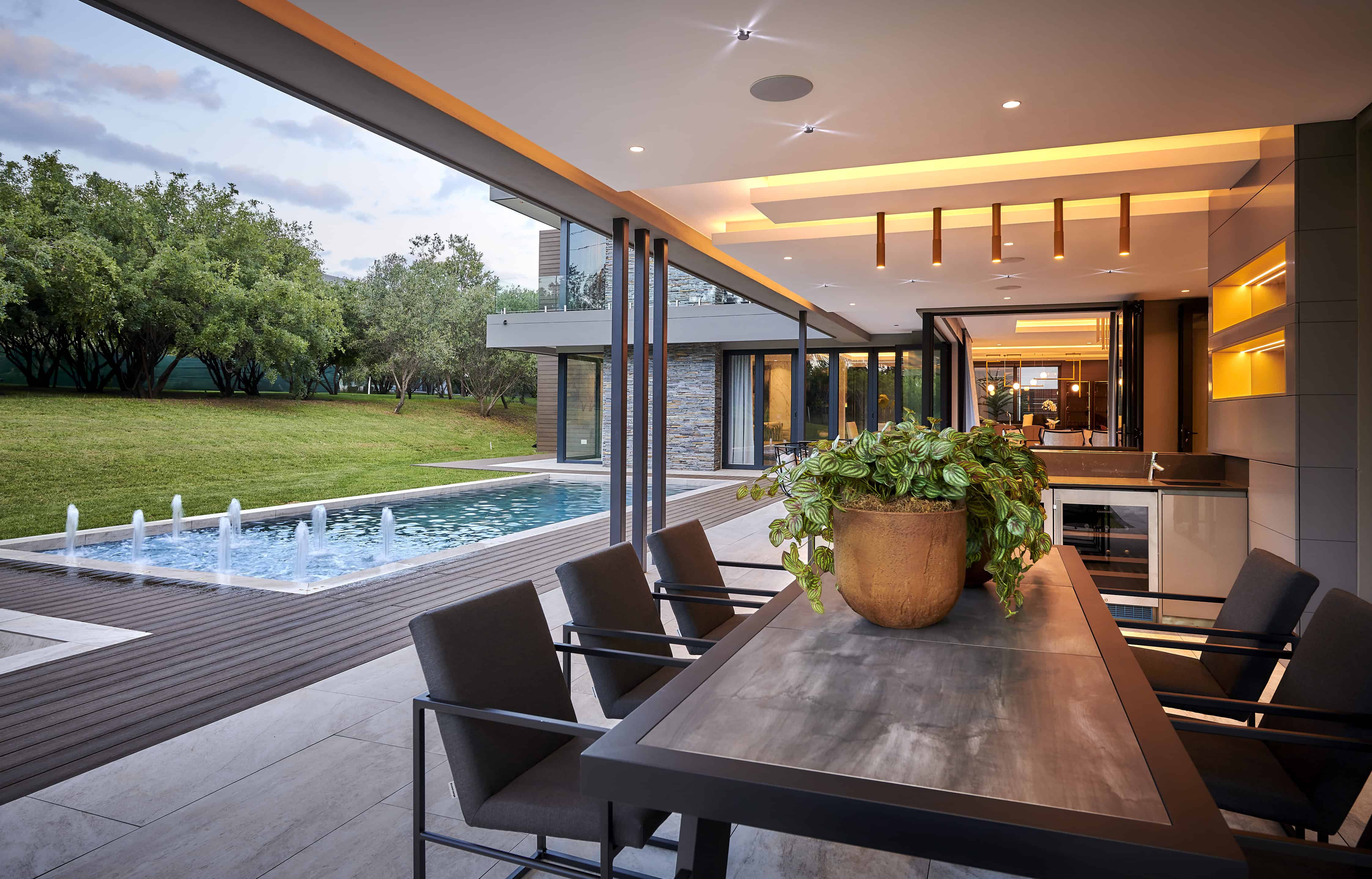 Covered patio dining space with wooden table, pendant lighting and pool view created by Interior Designer Johannesburg.
