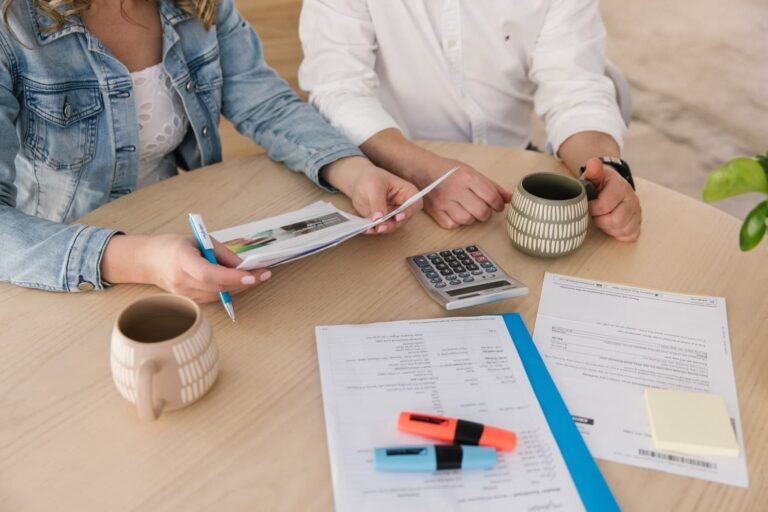 A young couple reviewing their finances at a table with bills, a calculator, and highlighters, considering debt consolidation to manage their repayments.