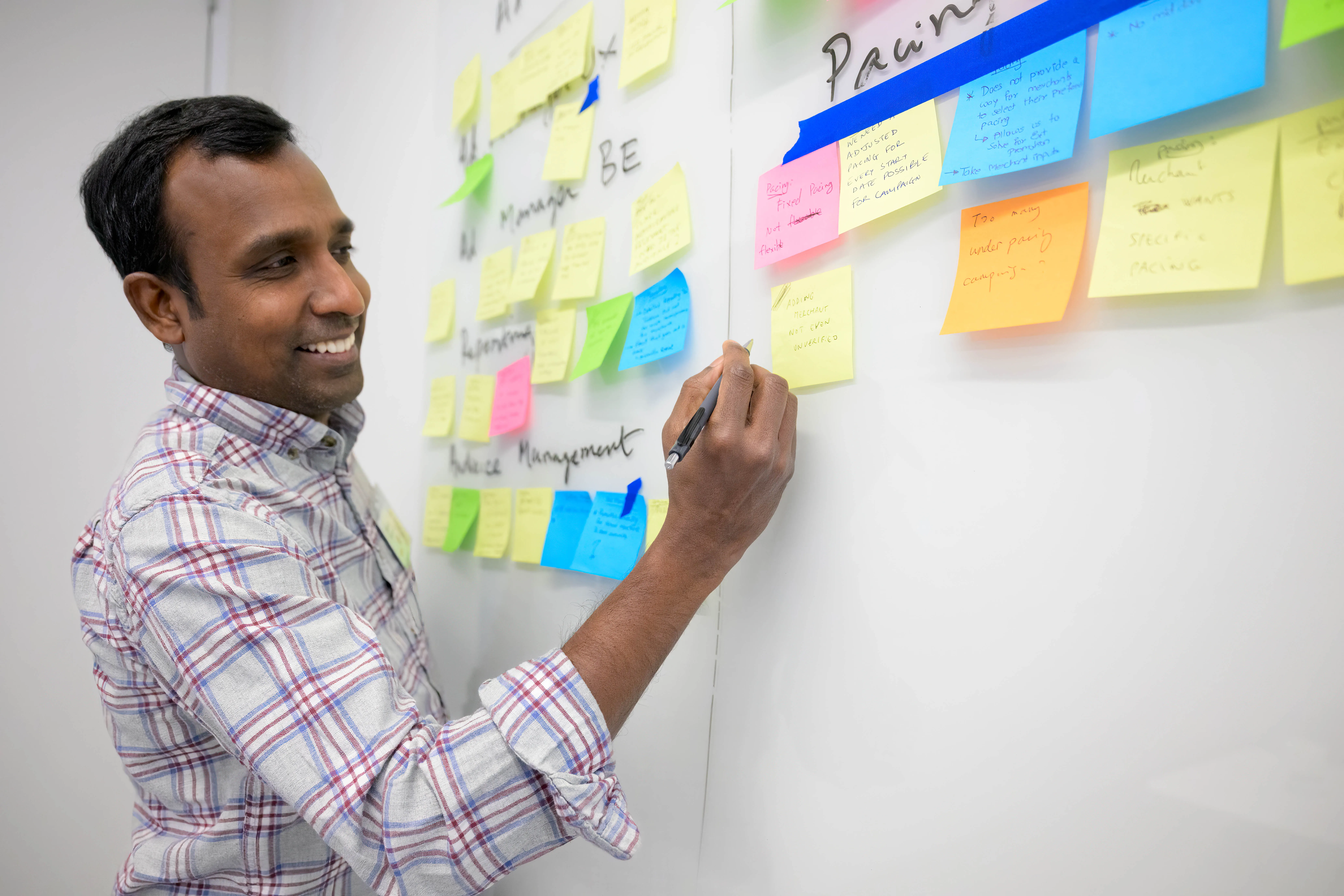 A man wearing a safety vest holds a laptop while standing next to another man wearing an orange helmet indoors.