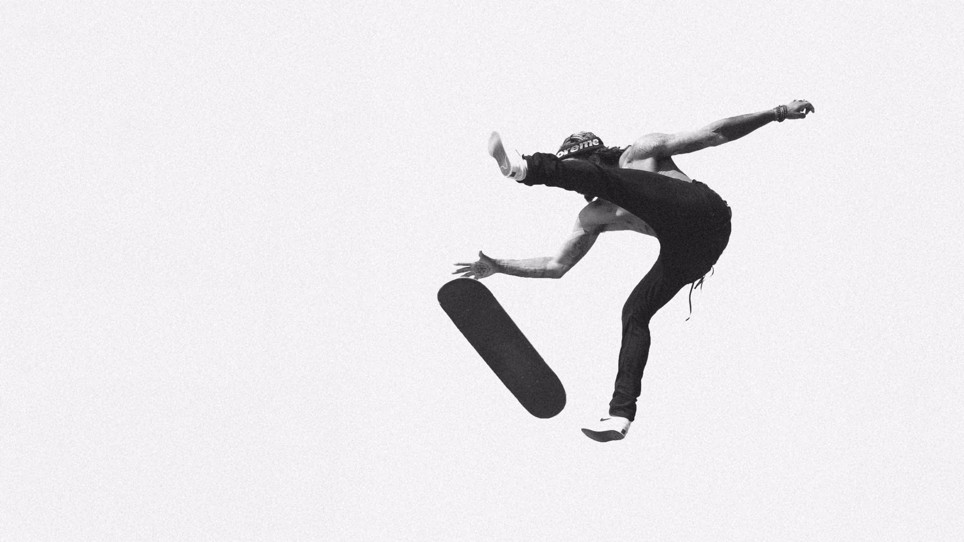 Black and white photo of a shirtless skateboarder mid-air performing a flip trick, with the skateboard flipping beneath him.