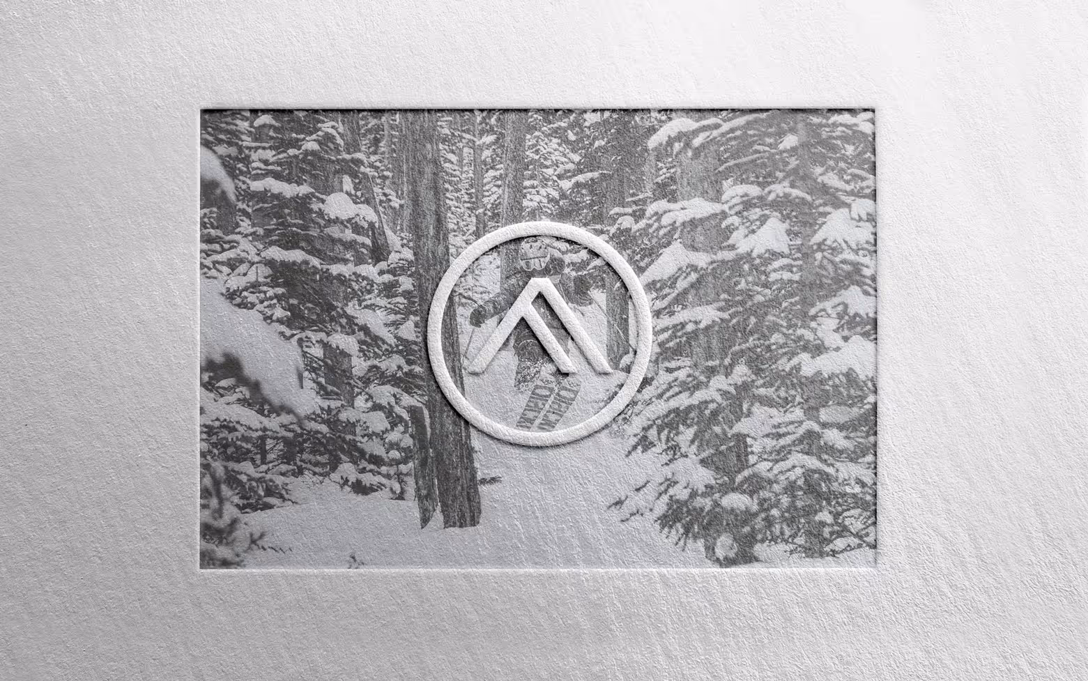 Peak icon and photo of a skier moving through deep powder snow between the trees, all embossed in a soft white felt paper.