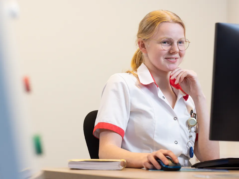 Verpleegkundige aan het werk vanachter haar bureau, kijkend op een scherm.