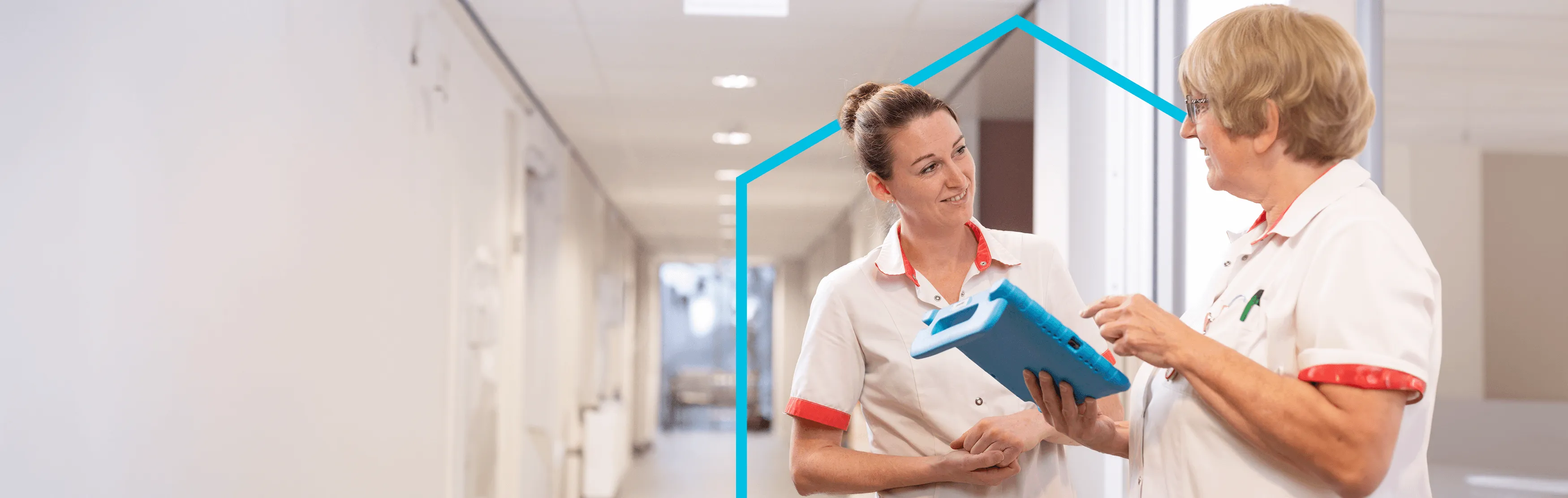 Twee verpleegsters met een ipad staan in de gang van een verzorgingshuis te overleggen