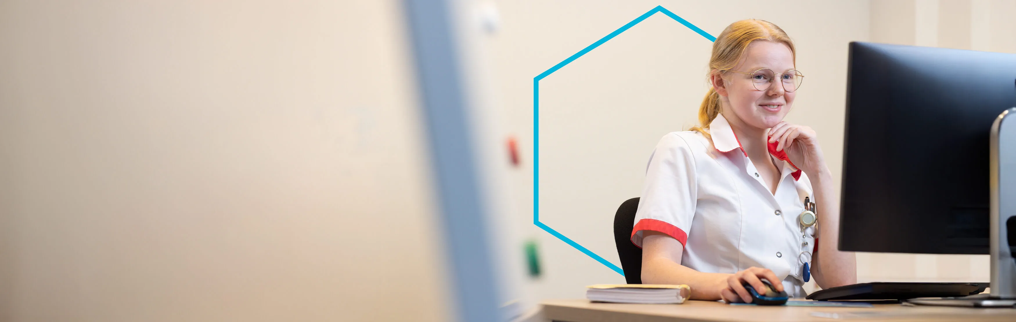 Zorgmedewerker zit achter haar werkplek en kijkt op een computerscherm.