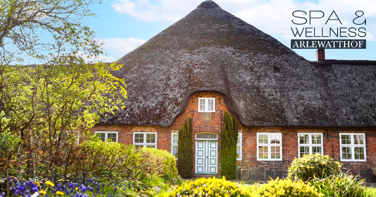 Traditionelles rotes Backsteinhaus mit großem, dunklem Reetdach und grünem Garten im Vordergrund unter blauem Himmel.