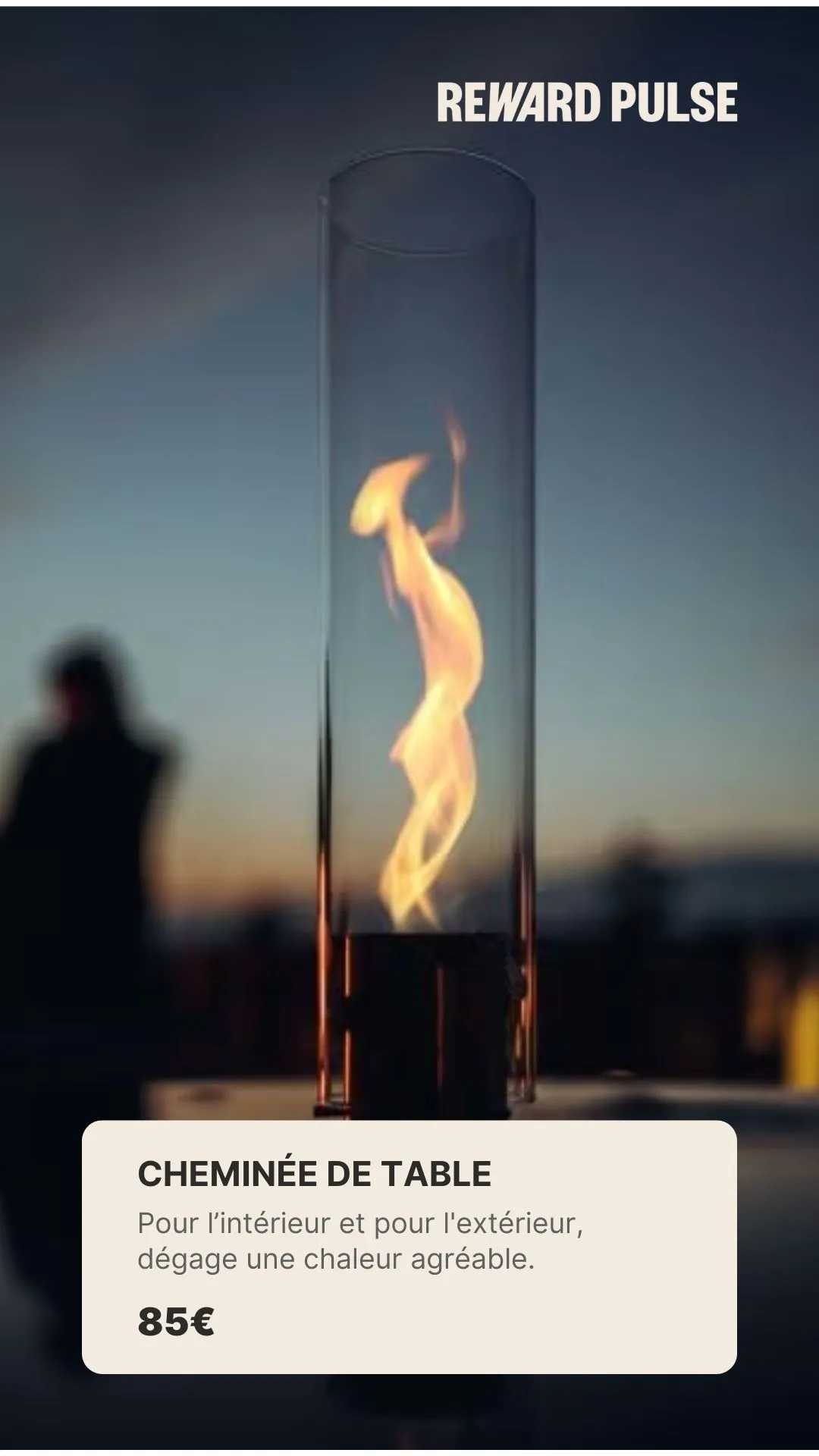 Modern glass table fireplace with a warm flame inside, blurred background at dusk.
