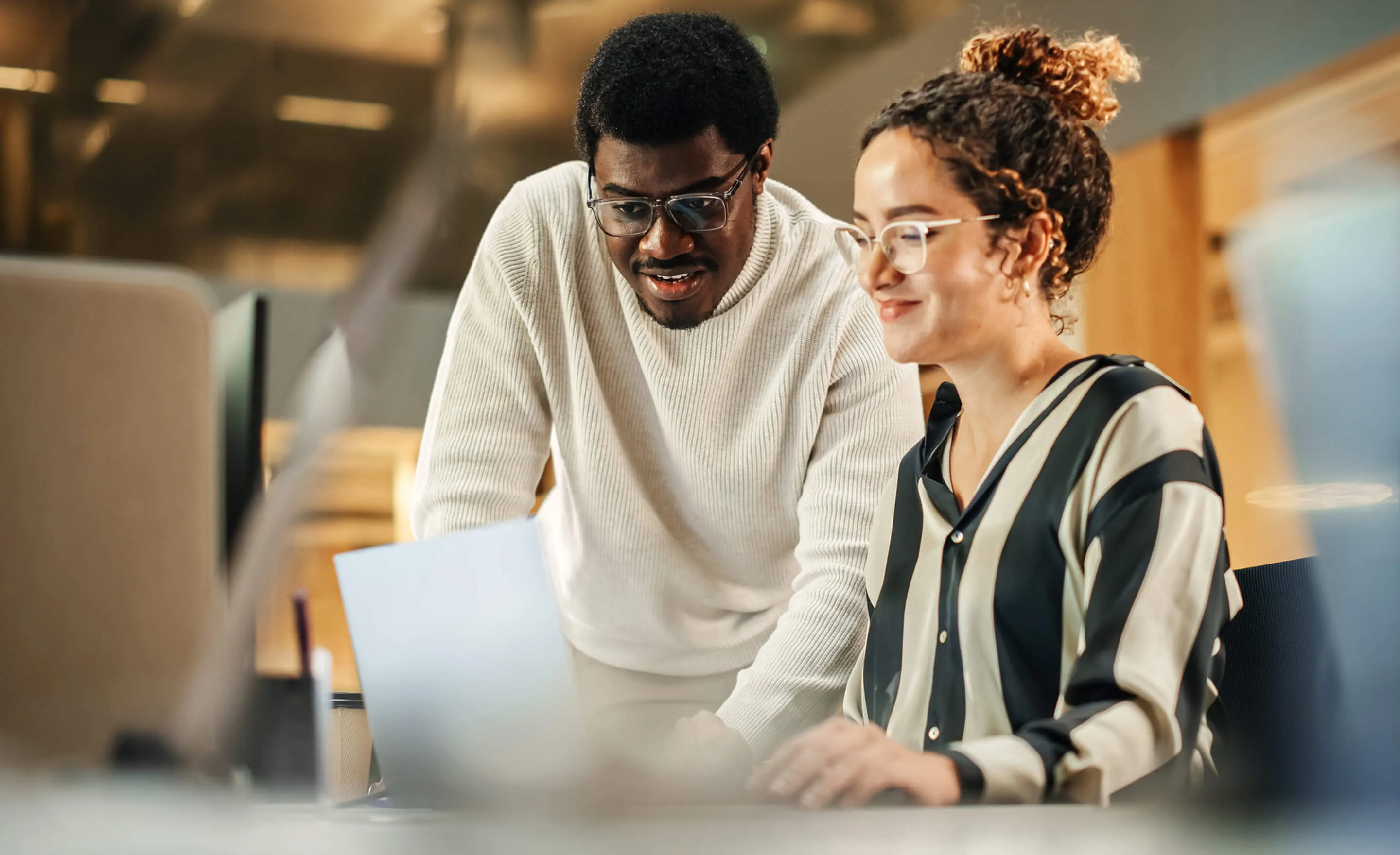 Two colleagues collaborating and looking at a laptop screen in a modern office.