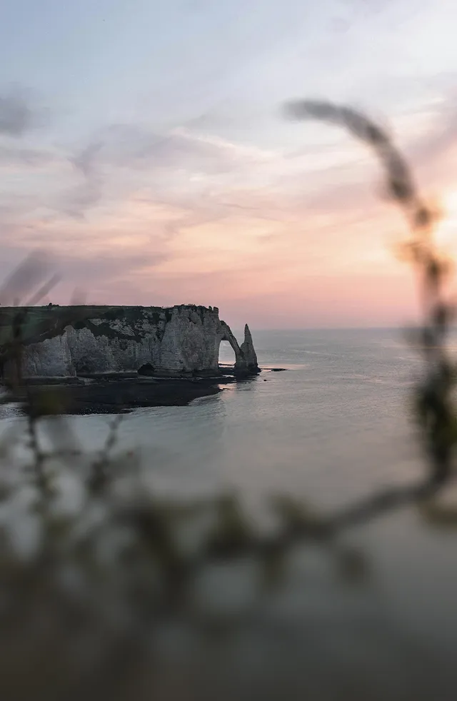 Cliff with natural arch formation overlooking calm sea at sunset with a pink and purple sky.