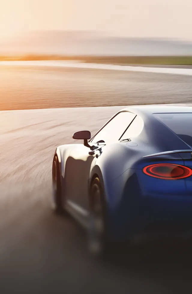 Rear side view of a blue sports car driving on a race track at sunset.