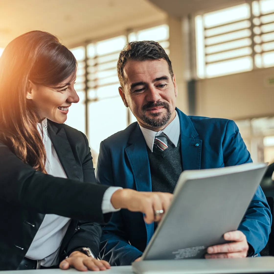 Two business professionals smiling and reviewing a document together in a bright office.