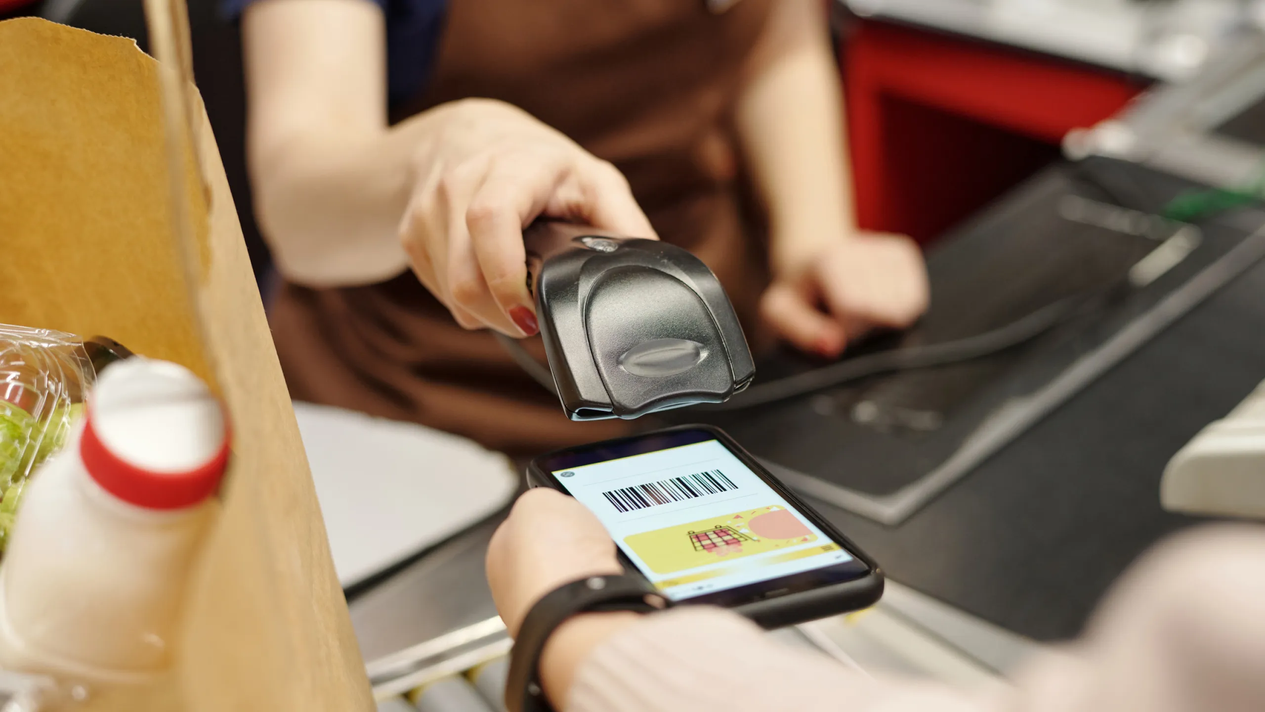 Cashier scanning a barcode displayed on a smartphone screen during checkout at a store.