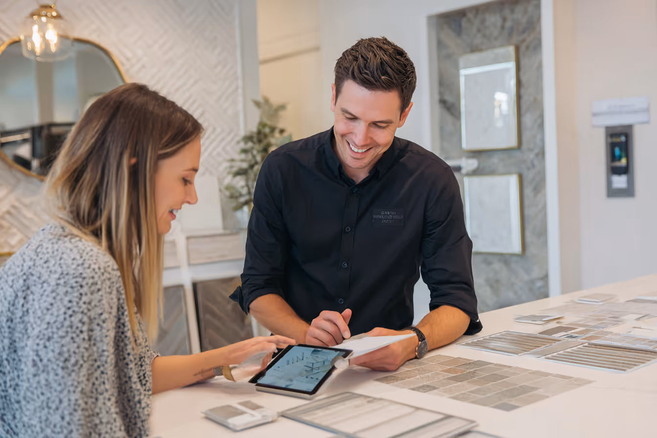 A clean, modern office scene where a client is reviewing a detailed mirror quote with a sales consultant. The consultant is showing a clear, itemized quote on a tablet or printed document, with visible line items for materials, edge finishes, delivery, and installation. The setting should feel professional and welcoming, with mirror samples or swatches on the table and a large mirror in the background. Subtle branding or signage can reinforce the transparency theme.