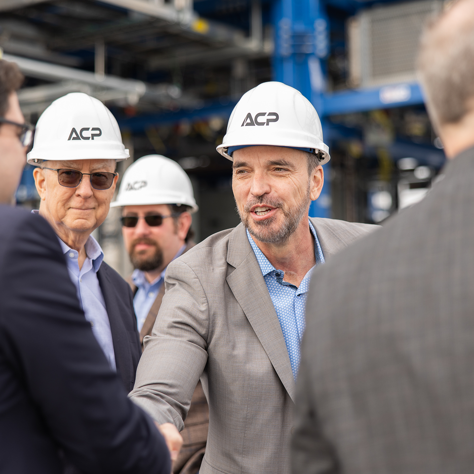 Men wearing ACP hard hats shaking hands inside an industrial facility.