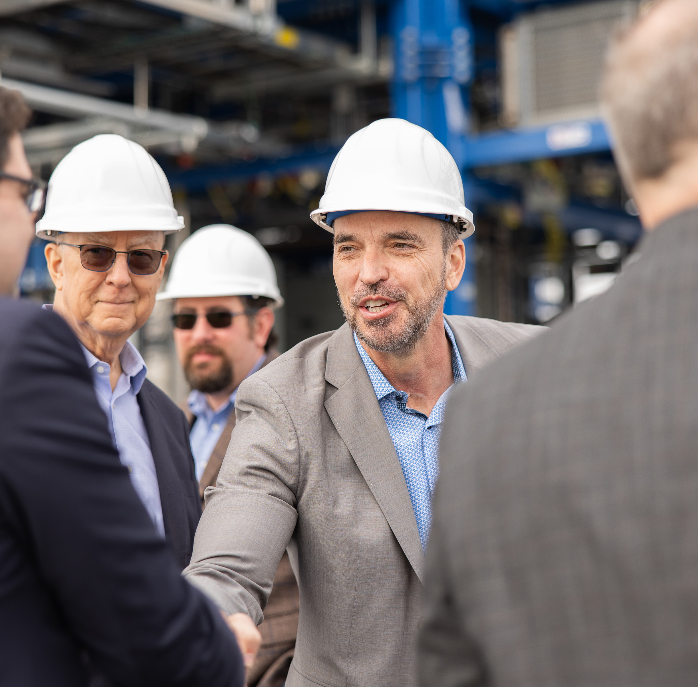 Men wearing ACP hard hats shaking hands inside an industrial facility.