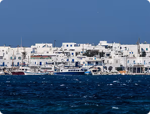 Coastal town with white buildings and boats docked by the deep blue sea under a clear sky.