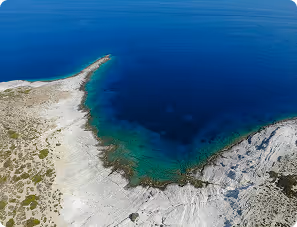 Aerial view of rocky coastline with clear blue water and a small peninsula extending into the sea.