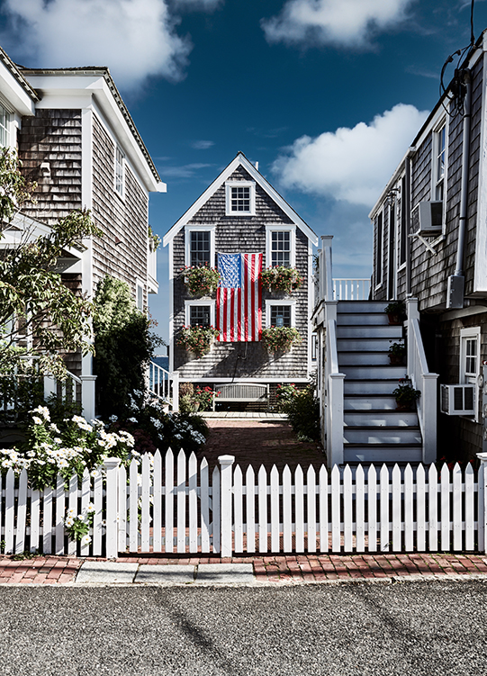 Beach house with american flag on it and white fence 