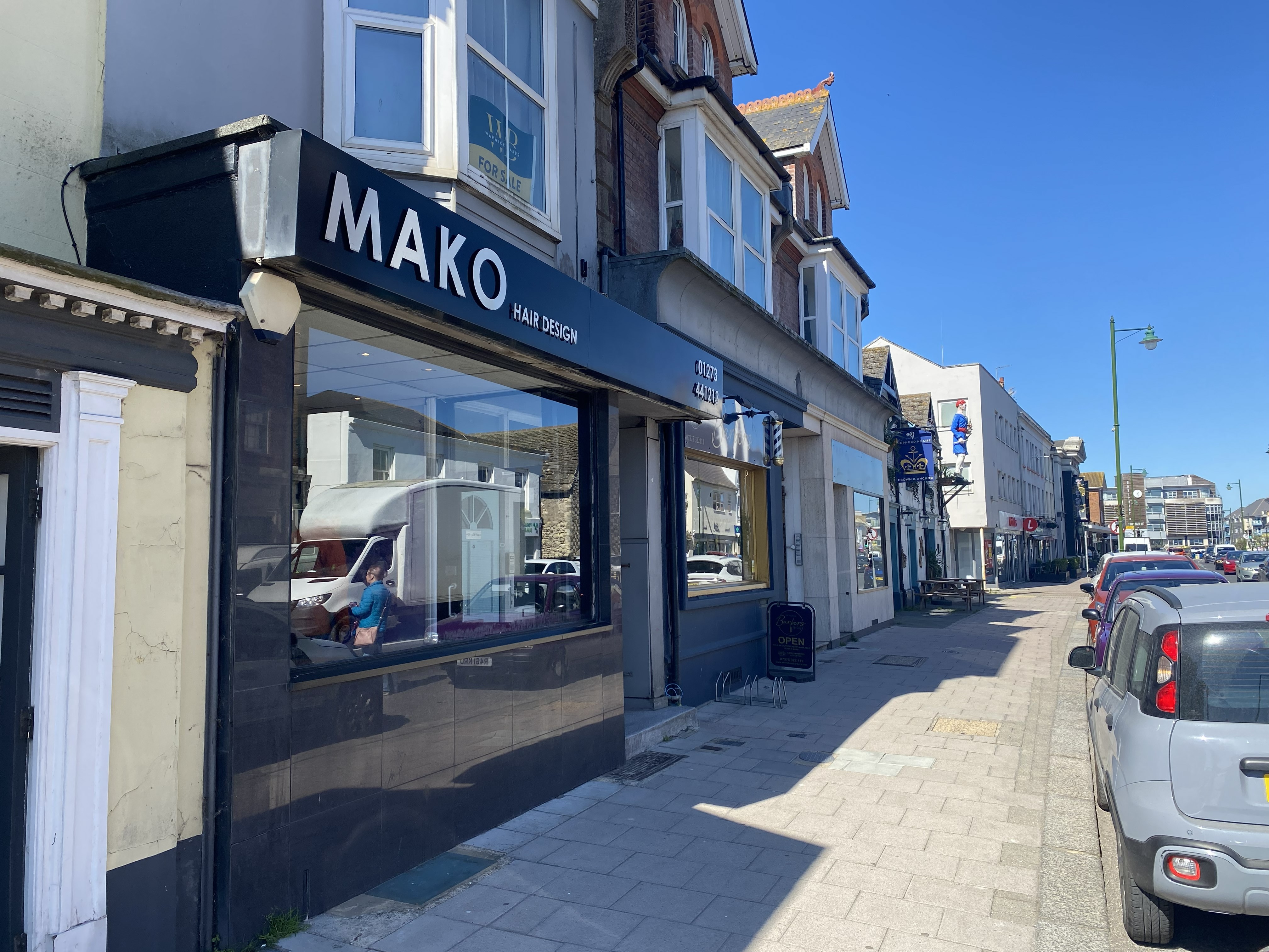 Street view of a row of buildings with MAKO Hair Design salon on the left under a clear blue sky.