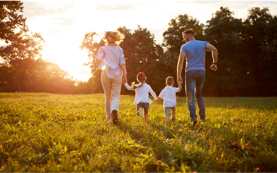 Mom, Dad and two children walking towards sunset at park.